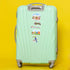 A mint green hard-shell spinner suitcase with travel stickers, including a Panama sticker, set against a solid bright yellow background.