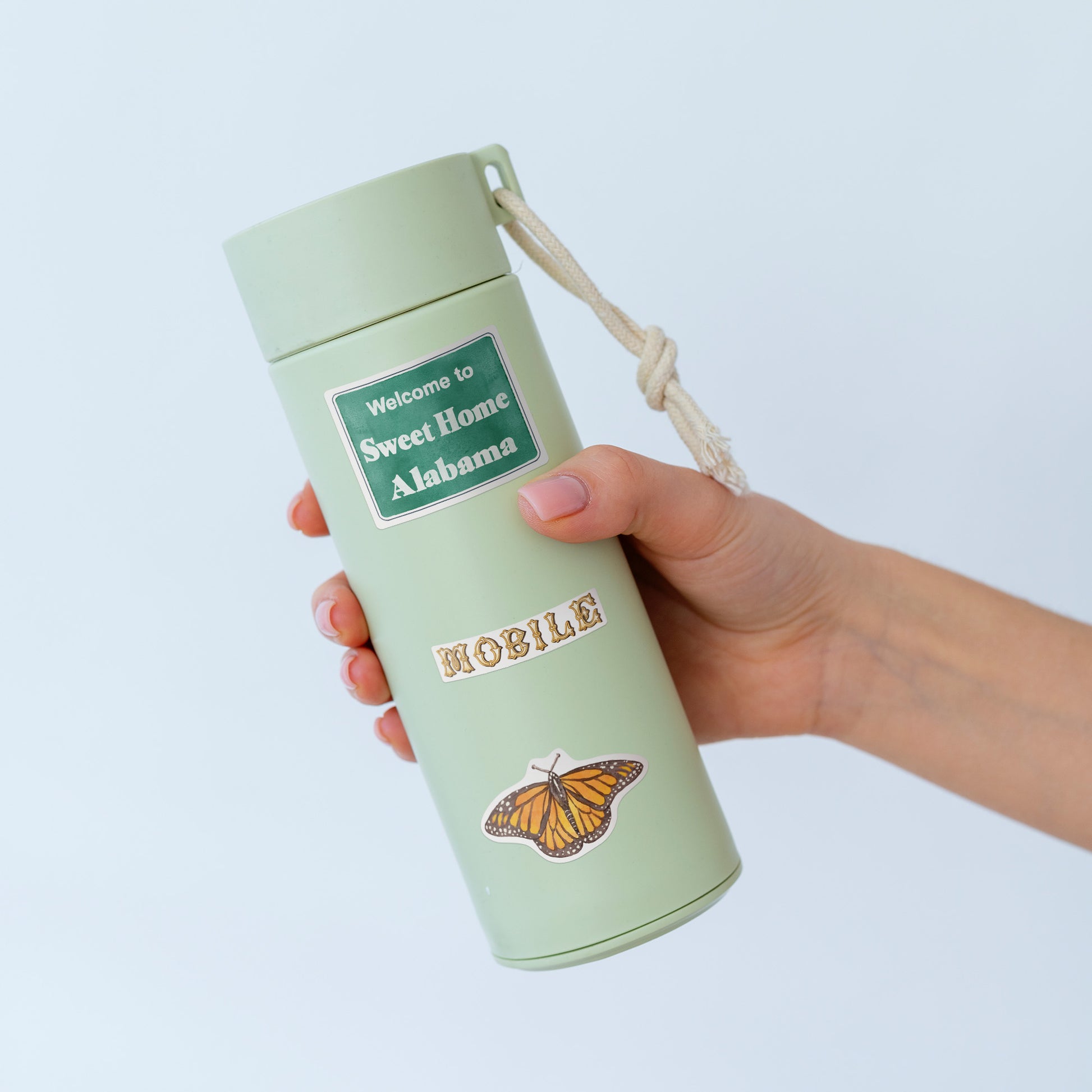 'Sweet Home Alabama' sign, 'MOBILE' and monarch butterfly stickers on a sage green water bottle