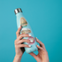 Gateway Arch, Loop Trolley and 'The Loop Delmar' badge stickers on a pale blue water bottle held in two hands.