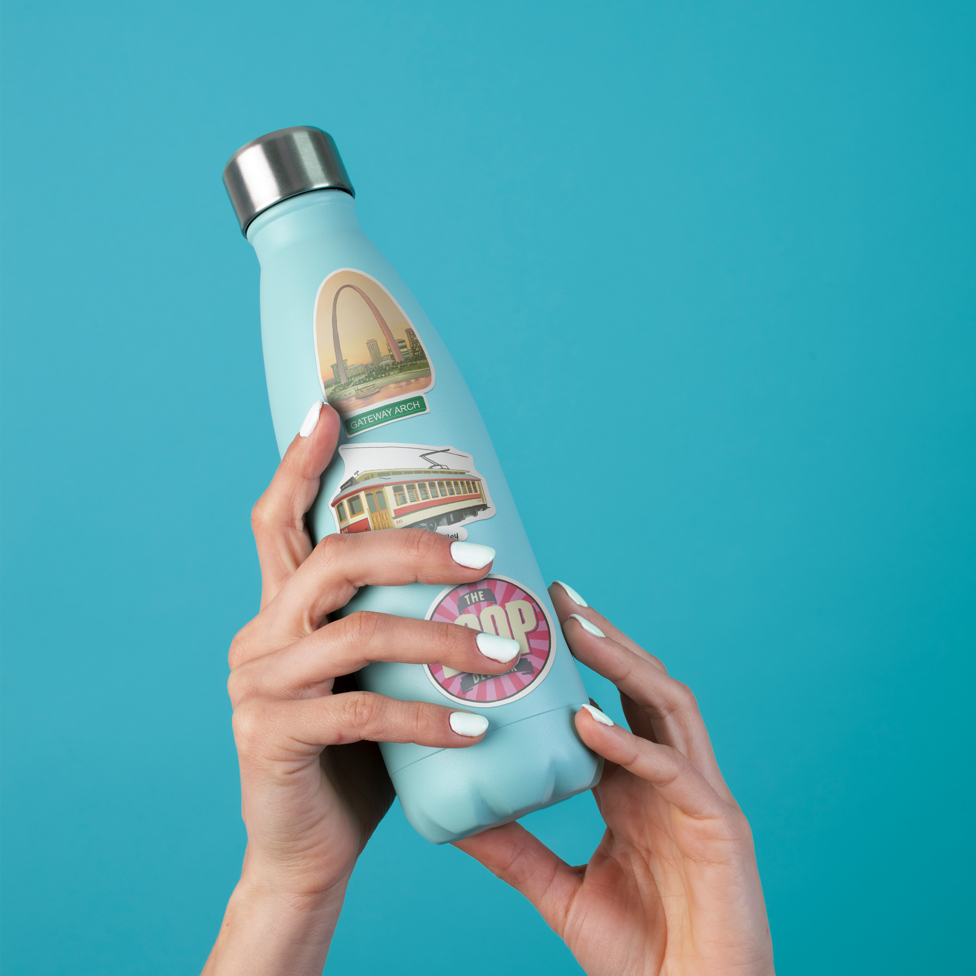 Gateway Arch, Loop Trolley and 'The Loop Delmar' badge stickers on a pale blue water bottle held in two hands.