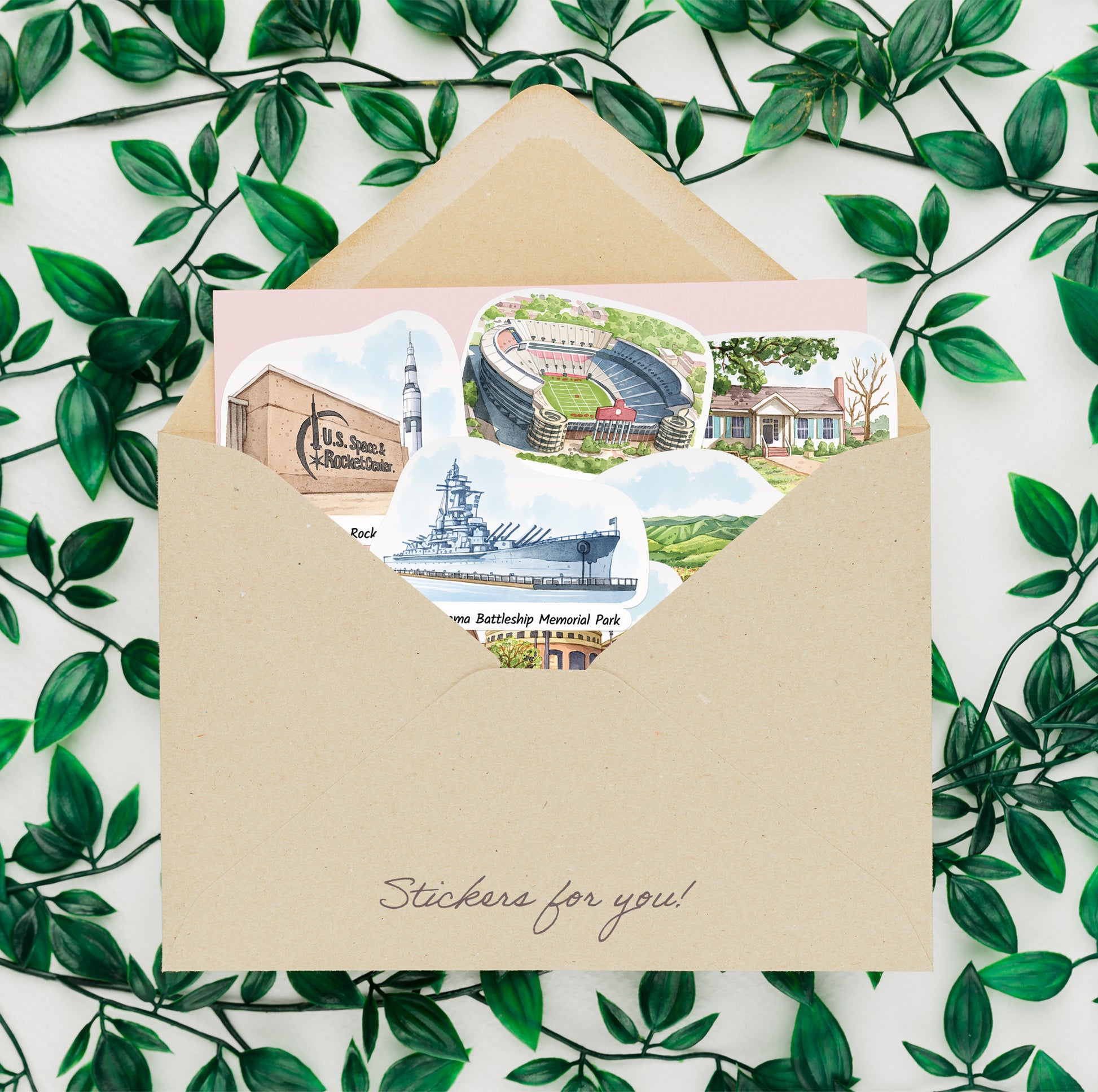 Alabama landmark stickers tucked in a kraft envelope framed by green leaves