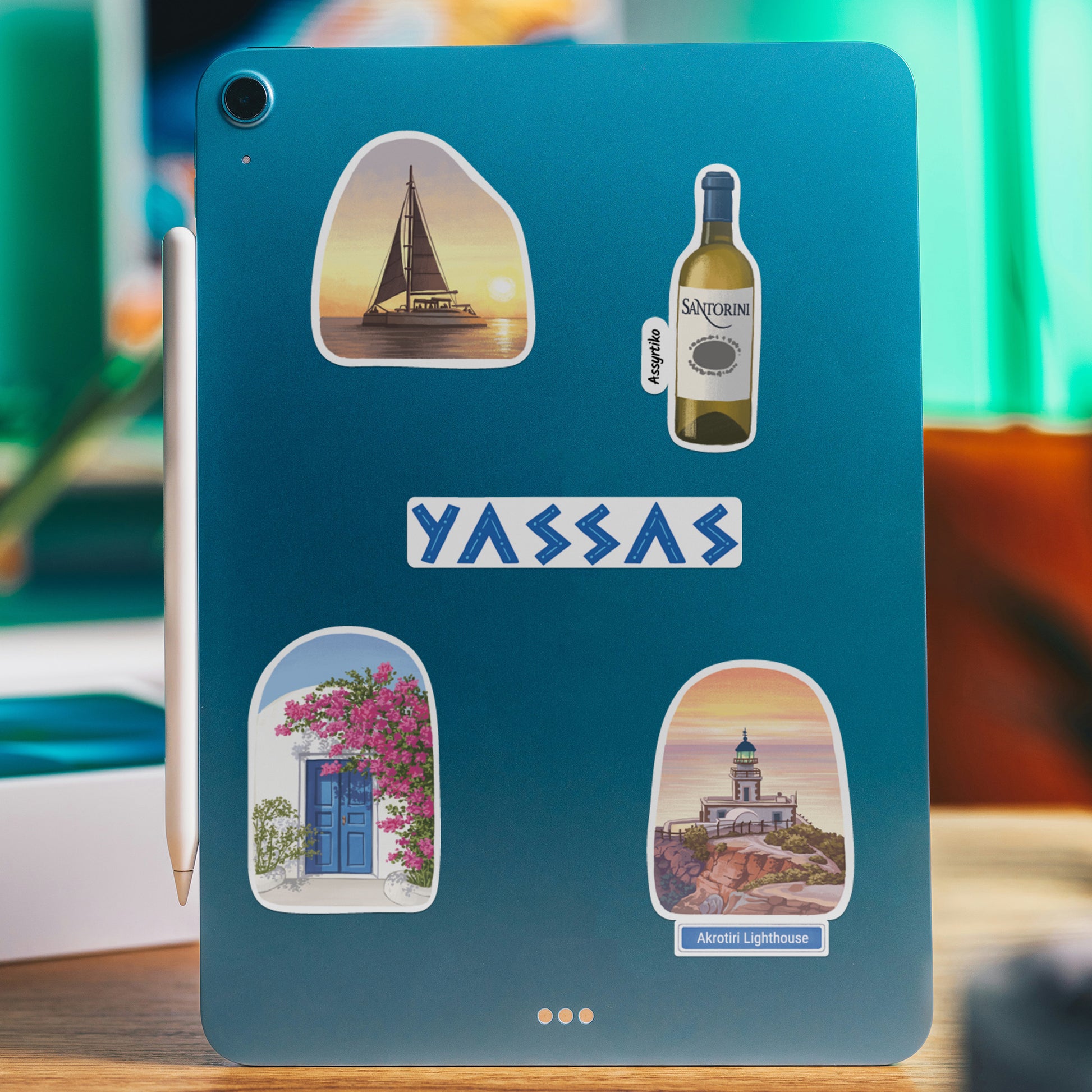 Blue tablet with Santorini stickers of a sunset bell tower, a wine bottle, 'Yassas' and a blue door