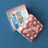 Pink polka-dot gift box holding Santorini stickers of Skaros Rock and Red Beach, on a navy background