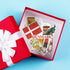 A red gift box with a white ribbon is open to reveal a set of Denmark-themed stickers, including the Danish flag, a map of Denmark, traditional figures, and landmarks, on a light blue background.