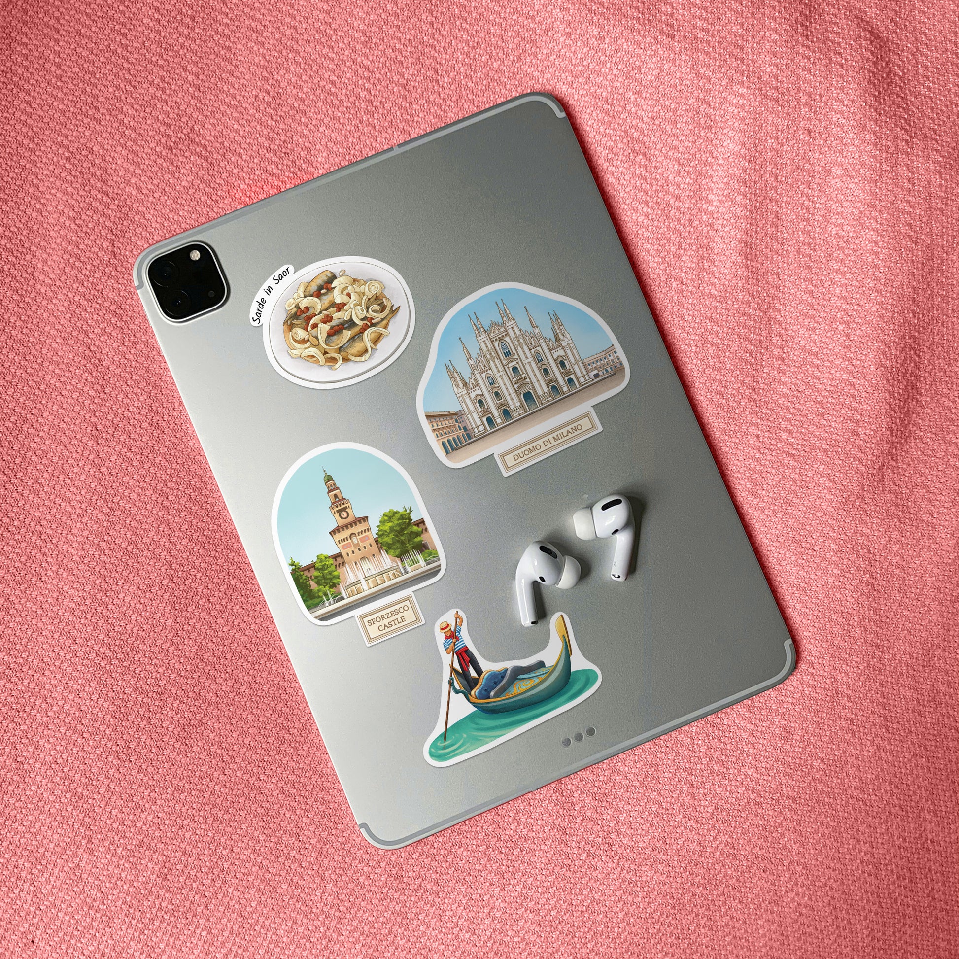 Duomo di Milano, Sforzesco Castle and gondola stickers on a silver tablet back beside earbuds