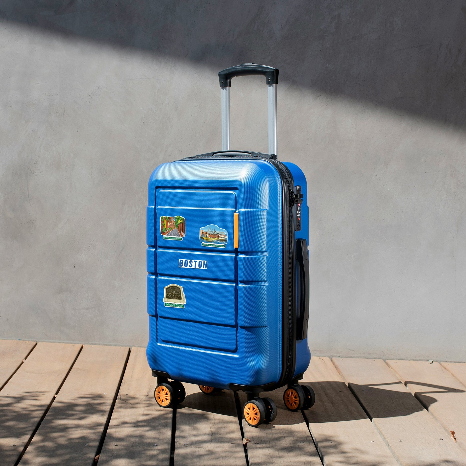 Fenway Park and 'Boston' stickers on a bright blue hardshell suitcase on a wooden deck