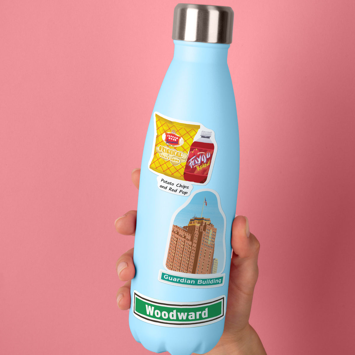 A light blue insulated water bottle with a silver cap, held in a hand against a solid pink background. The bottle features a sticker of Potato Chips and Red Pop, an illustration of the Guardian Building, and the name 'Woodward' on a green banner.