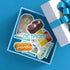 A square gift box with a blue interior displays a Detroit-themed sticker collage featuring the Detroit Public Library, Coney Dog Museum, a Red Pop soda bottle, and other local illustrations. A white gift box with a blue ribbon sits beside it on a bright blue background.