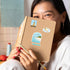 A woman holding a kraft notebook with Freedom Tower, key lime pie and Cape Florida Lighthouse stickers