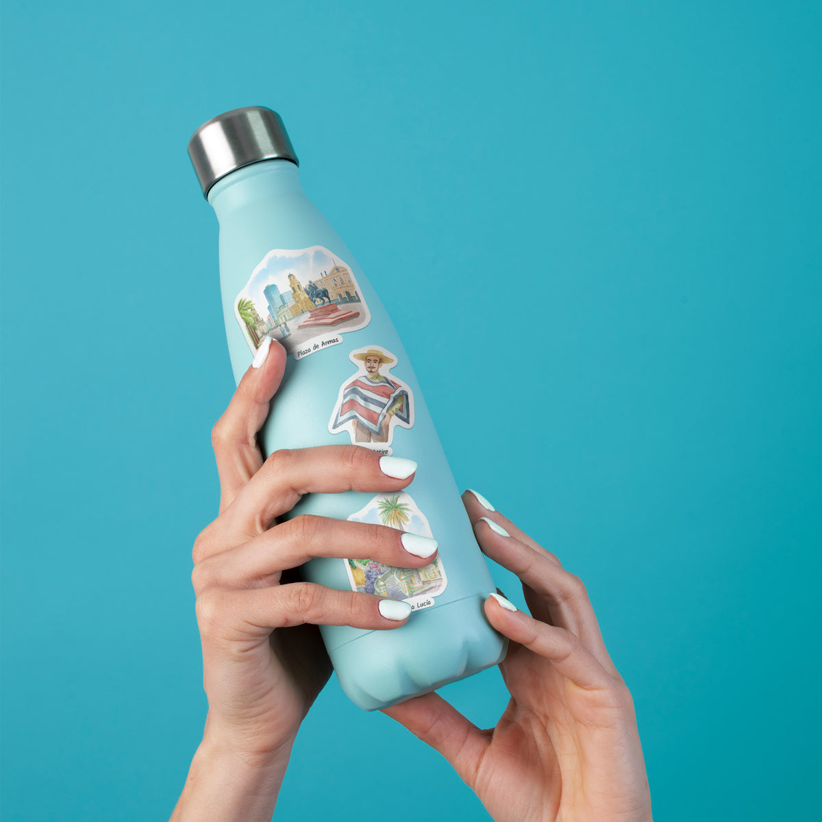 A light blue insulated water bottle with a stainless steel cap, held by two hands against a solid turquoise background. The bottle is decorated with three colorful travel-themed stickers.