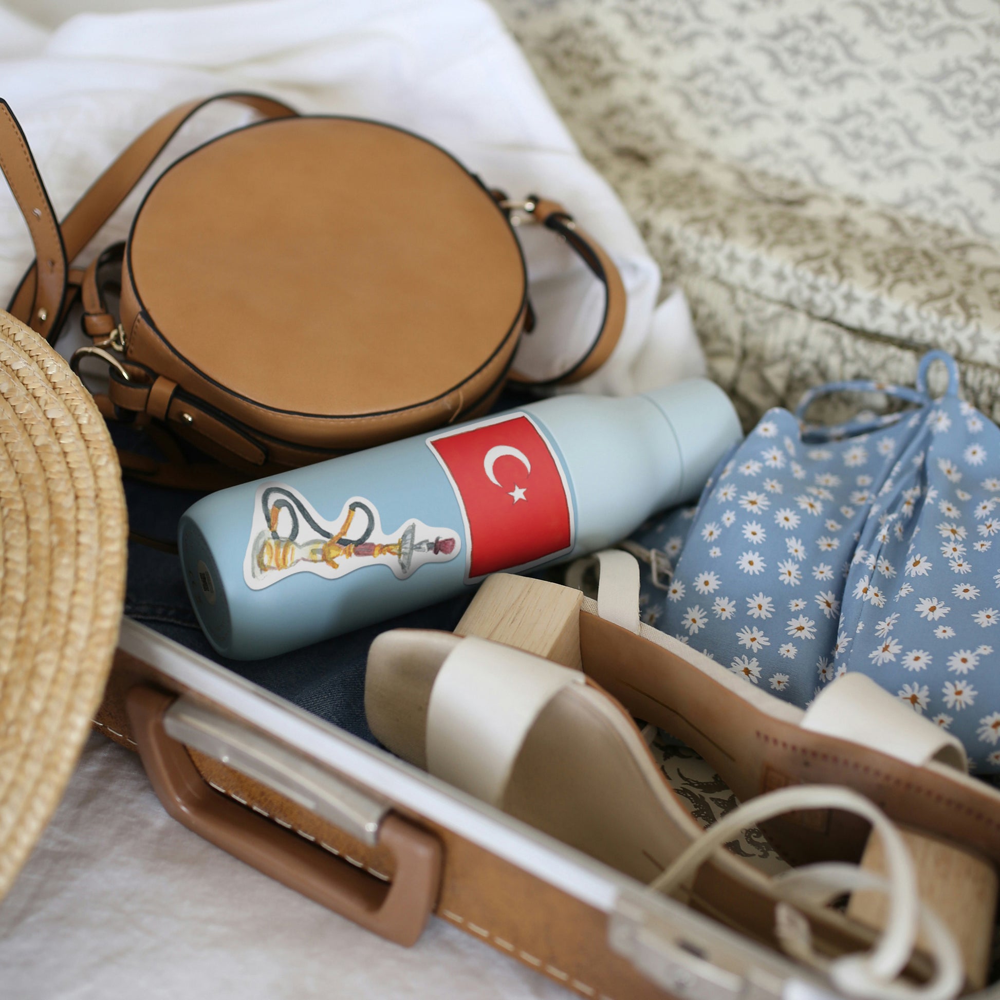 Turkish flag and hookah stickers on a pale blue water bottle packed in a bag with sandals